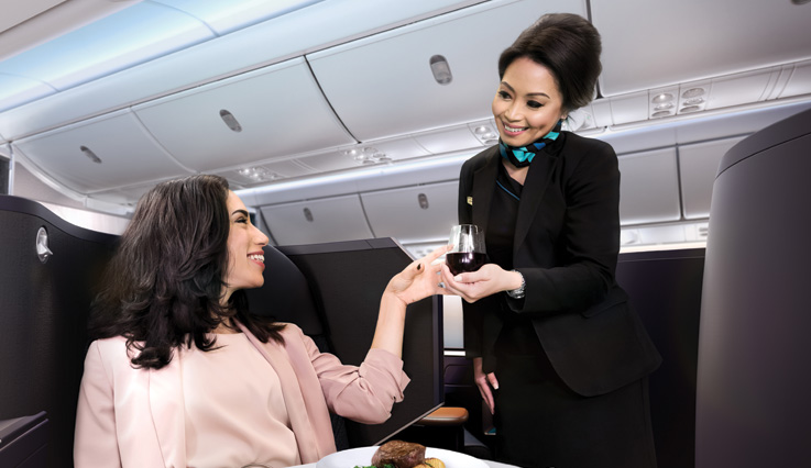 Auxiliar de vuelo de WestJet sirviendo una bebida alegremente a una mujer en la cabina Business