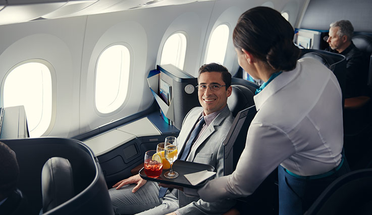Auxiliar de vuelo sirviéndole bebidas a un hombre sentado en la cabina Business