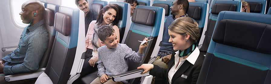 WestJet flight attendent in aisle positively interacting with seated child pretending to fly toy plane in Economy cabin