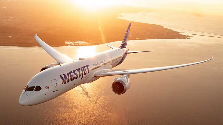 WestJet Dreamliner flying over coast at sunset