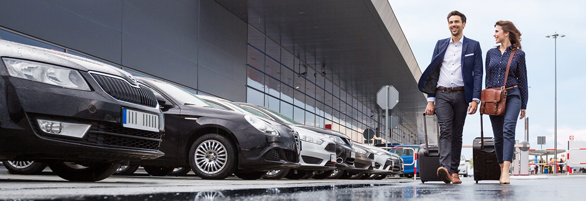 Un homme et une femme transportant des valises marchent vers leur voiture garée à l'aéroport.