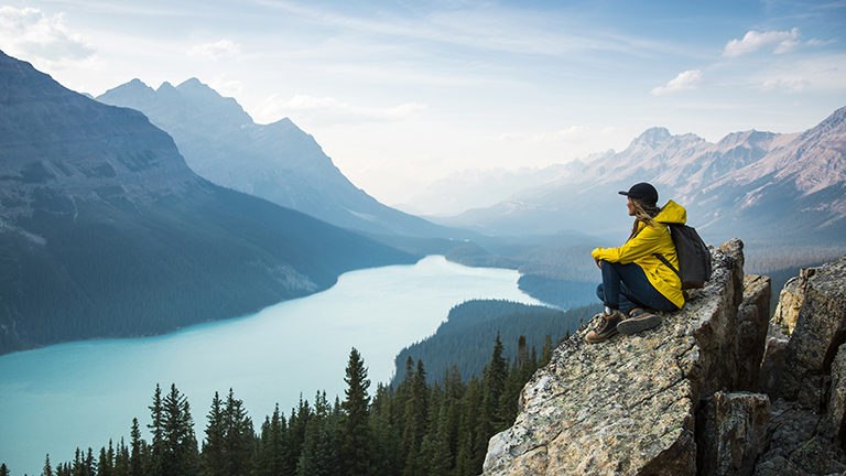 A young woman in a yellow jacket sitting on a rock overlooking Peyto Lake.