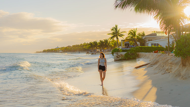 Une femme marche sur la plage au coucher du soleil