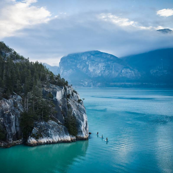 Mountainous coastline with paddle boarders in the water.