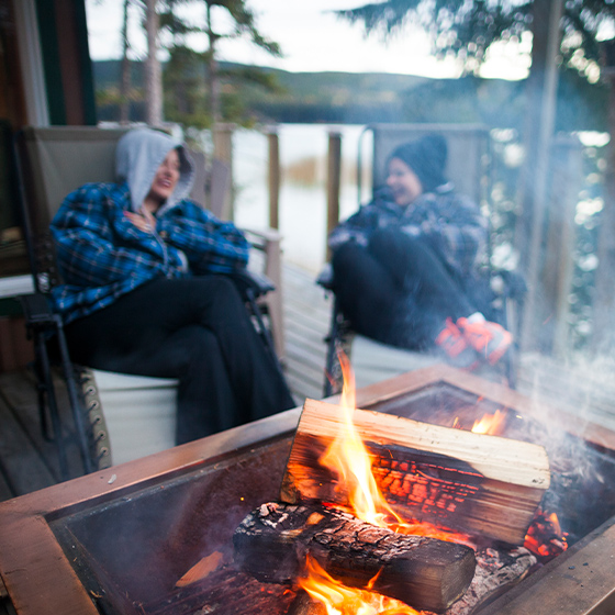 Two people sitting around a campfire on a deck lakeside
