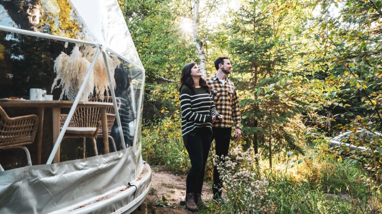 Couple looks out into the forest beside their geodome at Elk Island Retreat