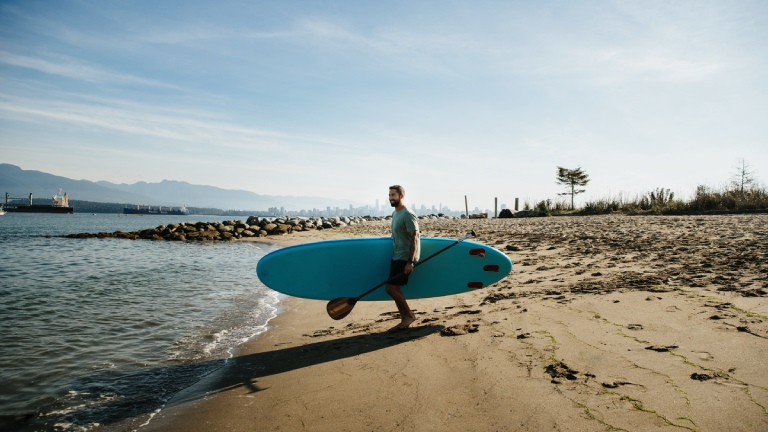 Un homme transportant une planche de surf sur une plage de Vancouverr
