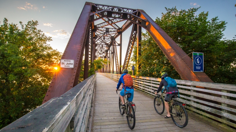 Two people riding bikes across bridge in Fredericton