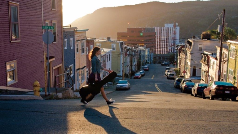 Une femme traversant la rue portant un étui de guitare à St. John’s