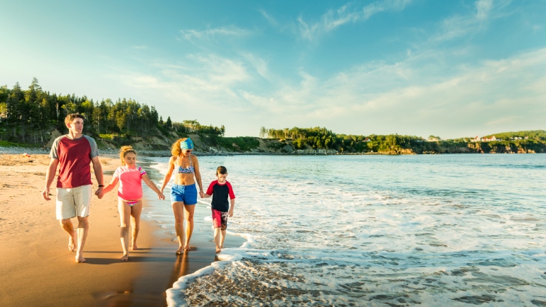 Une famille marche sur la plage du cap Breton