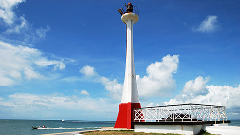 Red and white lighthouse with boats passing by in Belize City