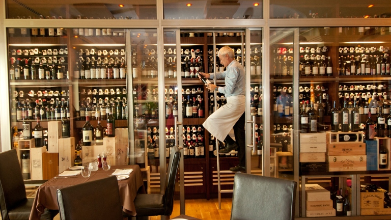 Homme sur une échelle prenant une bouteille dans la cave à vin du restaurant Luca