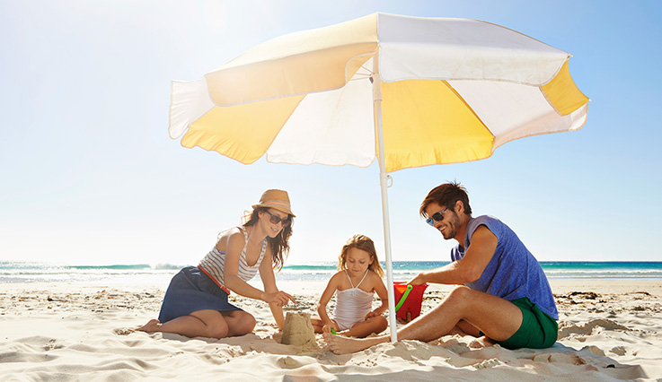 Famille qui fait un château de sable sous un parasol sur une plage.