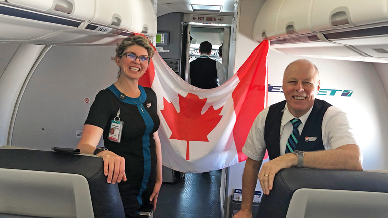 Man and woman flight attendants with Canadian flag behind them