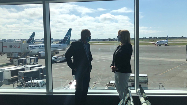 Ed et Tamara devant des fenêtres dans une aire d'embarquement à YVR avec des avions WestJet sur l'aire de trafic