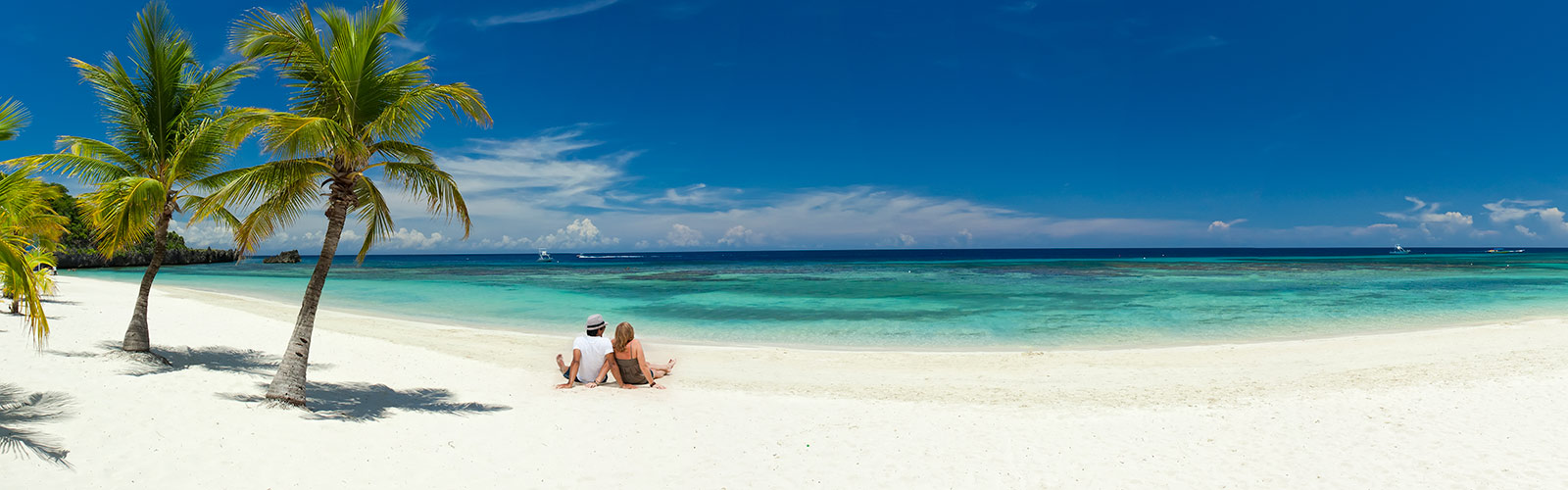 Man and woman looking at ocean while sitting on white sand beach