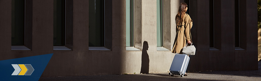 Traveller in trench coat with luggage, walking from shadows into the light.