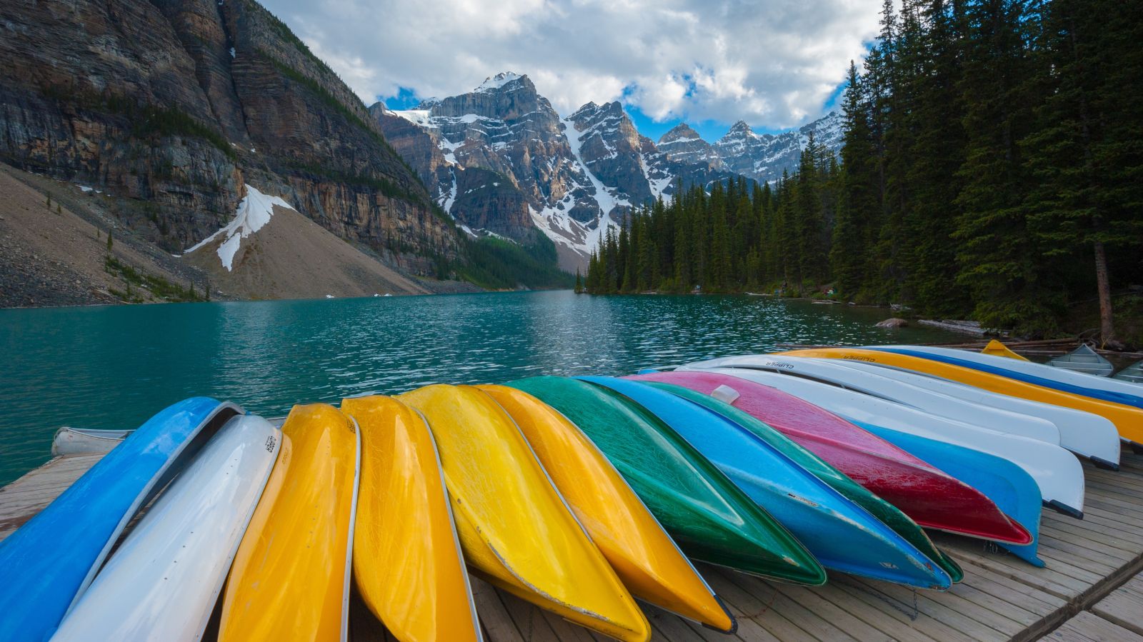Canoes on a dock in front of a lake and mountains.