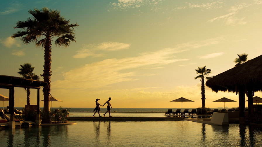 couple walking along the pool at sunset