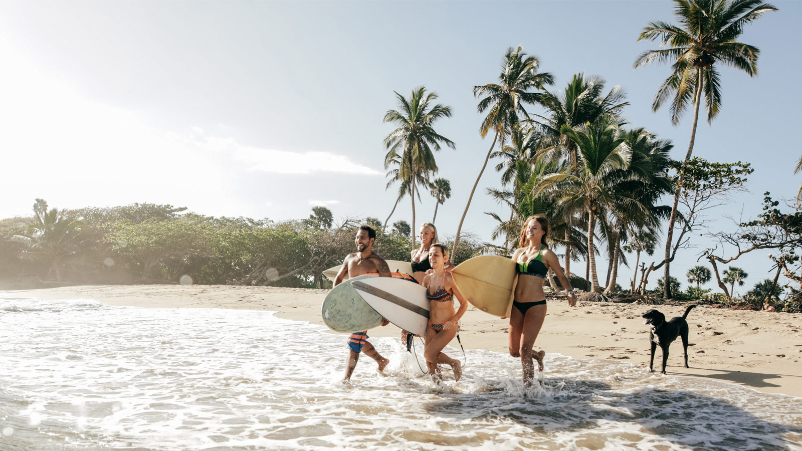 Friends running towards ocean with surfboards