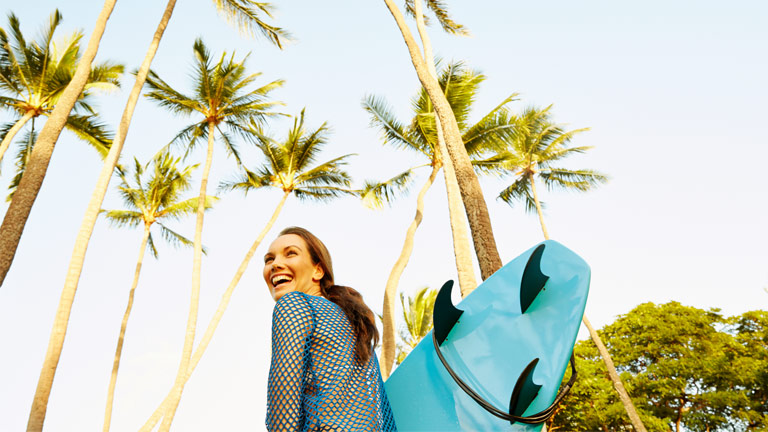 Person smiling while carrying surfboard on all-inclusive vacation
